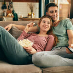 Young happy couple relaxing while watching TV and eating popcorn at home.